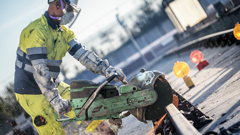 一名佩戴安全设备的工人使用大型电锯切割钢轨。.