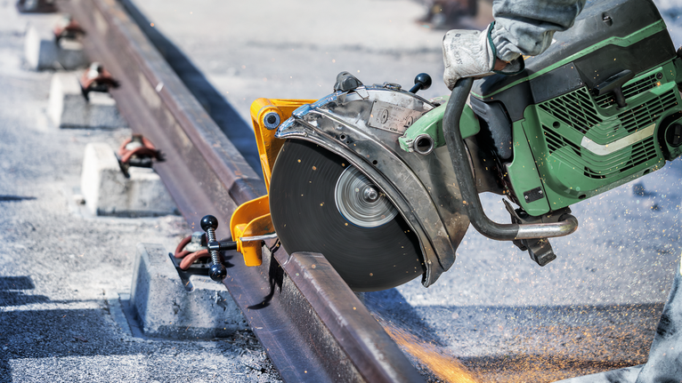 切割锯切割钢轨，工人佩戴安全设备。.