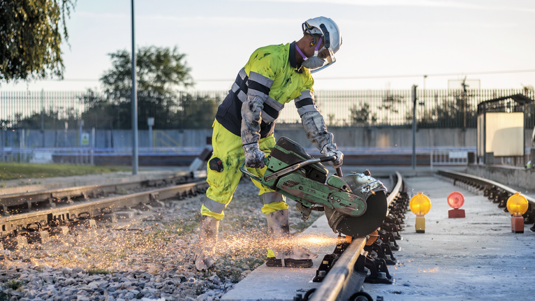 一名佩戴安全设备的人正在用电锯切割铁轨。