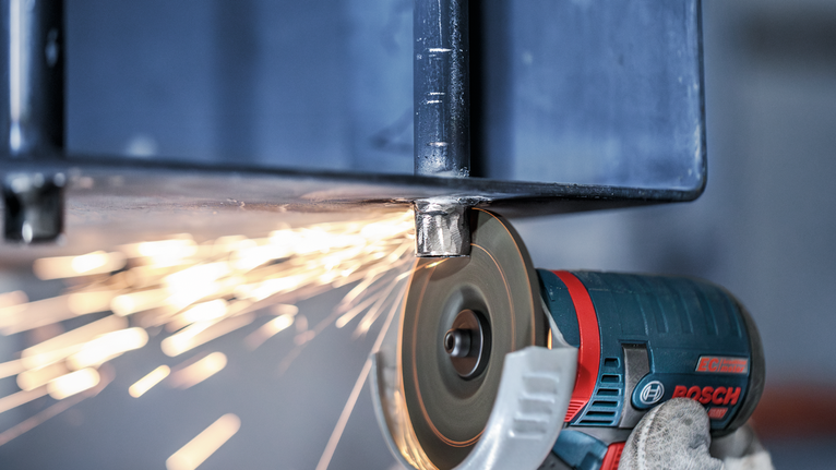 戴着手套、穿戴着安全设备的工人用角磨机打磨金属梁，产生火花。.