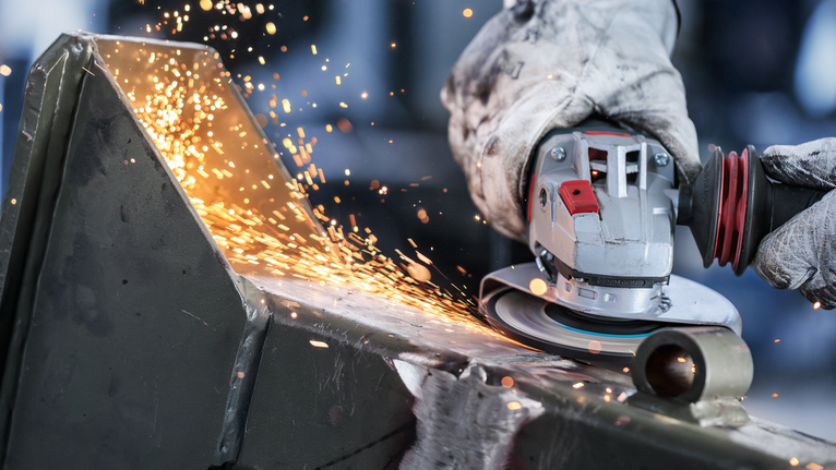 佩戴安全设备的人员用角磨机研磨金属，产生火花。