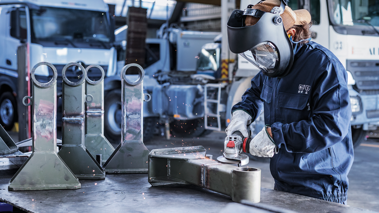 佩戴安全设备的人员在工业环境中研磨金属零件。