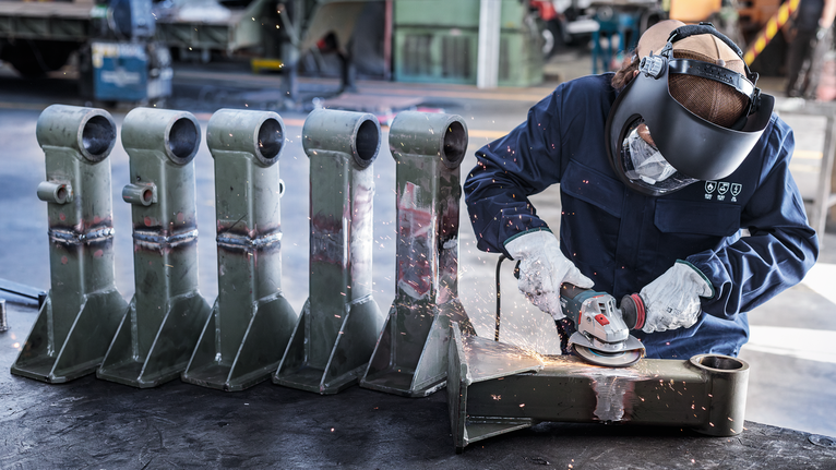 车间内，佩戴安全设备的人员正在研磨金属零件，产生火花。