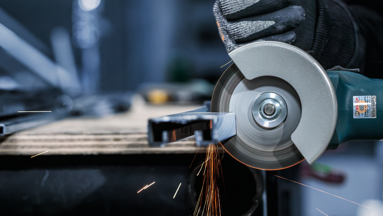 佩戴安全设备的人使用角磨机切割金属，产生火花。