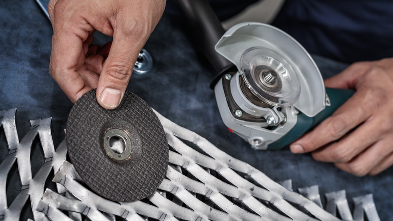 工人正在金属格栅附近的电动工具上更换砂轮。.