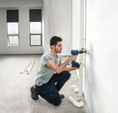 一个人在一间明亮的、未完工的房间里钻孔安装管道。.