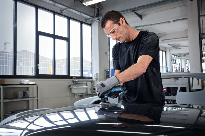 佩戴安全设备的人员正在使用随机轨道打磨机打磨汽车车顶。.