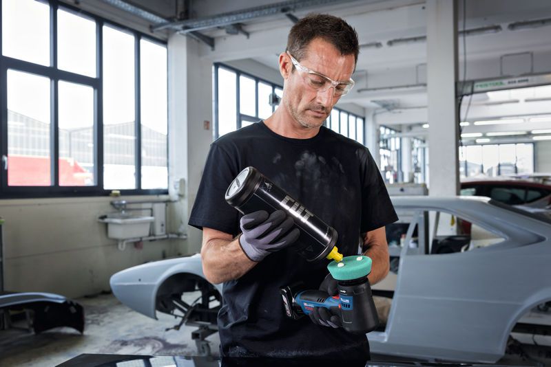 一名佩戴安全设备的人员在汽车修理厂内对电动抛光机进行抛光。.