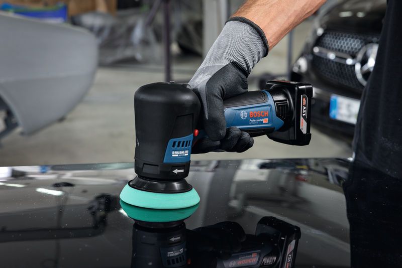 一名佩戴安全设备的人员正在使用无绳抛光机抛光汽车表面。.