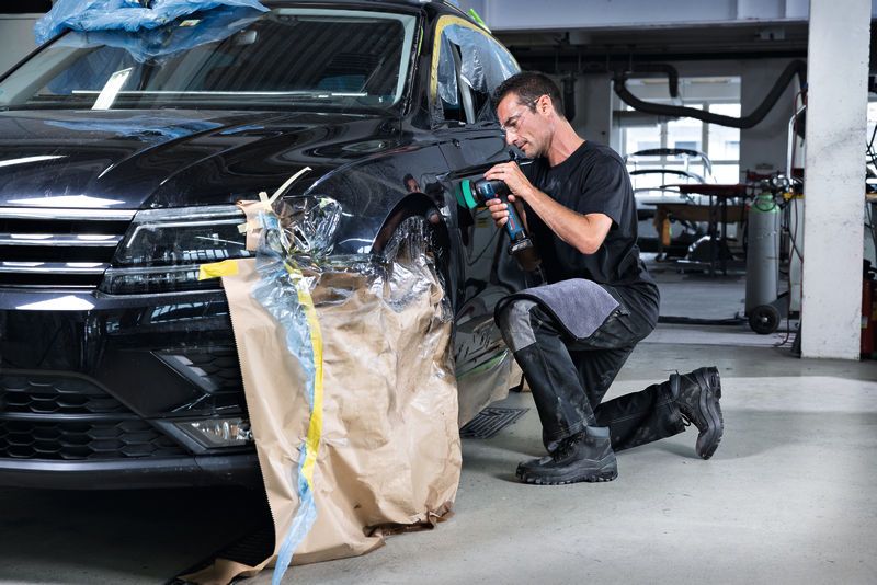 汽车修理店里，一名佩戴安全设备的人员正在使用抛光机抛光汽车挡泥板。.