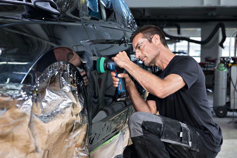 一名佩戴安全设备的人员正在使用无绳工具擦拭车门。.