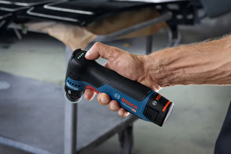 一个人在车间里拿着一台无绳随机轨道砂光机。.