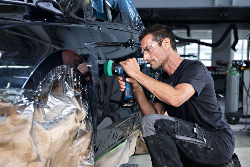 一名佩戴安全设备的人员正在使用无绳工具擦拭车门。.