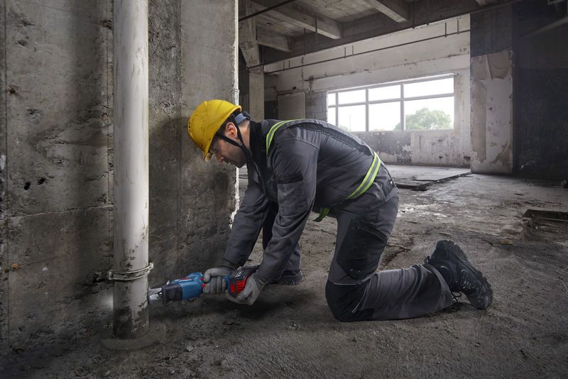 一名佩戴安全设备的人员使用往复锯切割混凝土墙附近的管道。.