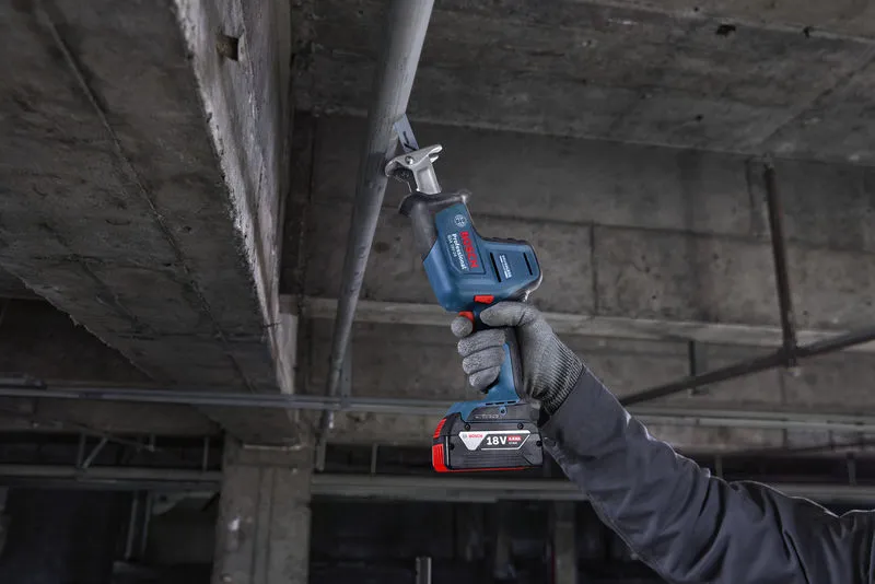 一名佩戴安全设备的人员正在用往复锯切割头顶上的金属管道。.