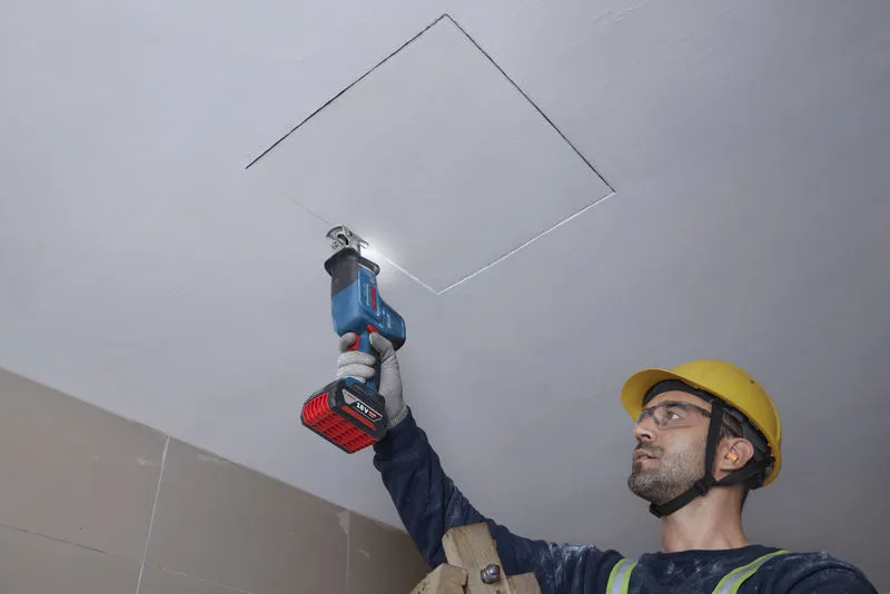 一名佩戴安全设备的人员正在用往复锯切割天花板。.