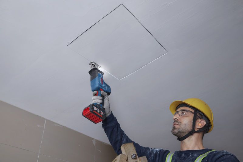 一名佩戴安全设备的人员正在用往复锯切割天花板。.