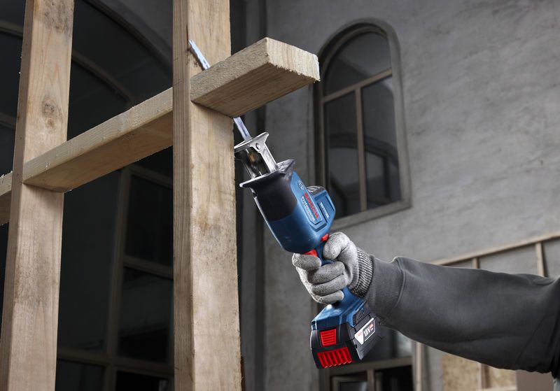 一名佩戴安全设备的人员使用往复锯切割木梁。.