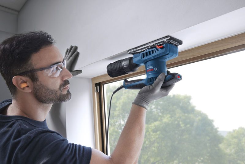 一名佩戴安全设备的人员正在使用轨道砂光机打磨窗框。.