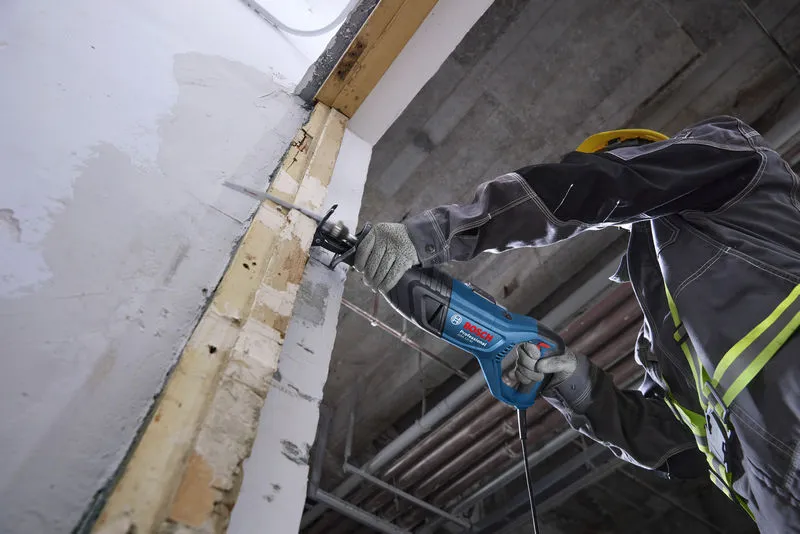 一名佩戴安全设备的人员使用往复锯切割墙壁。.