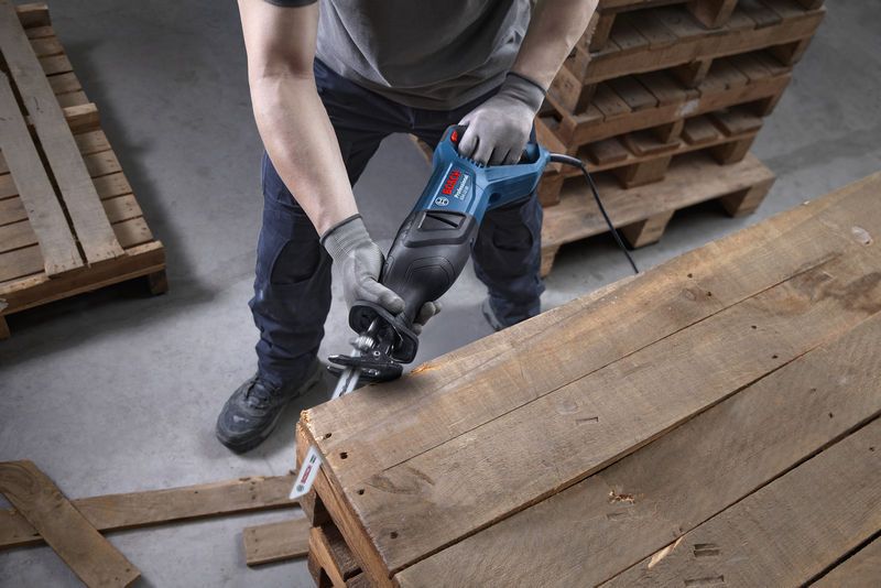 一名佩戴安全设备的人员使用往复锯切割木托盘。.