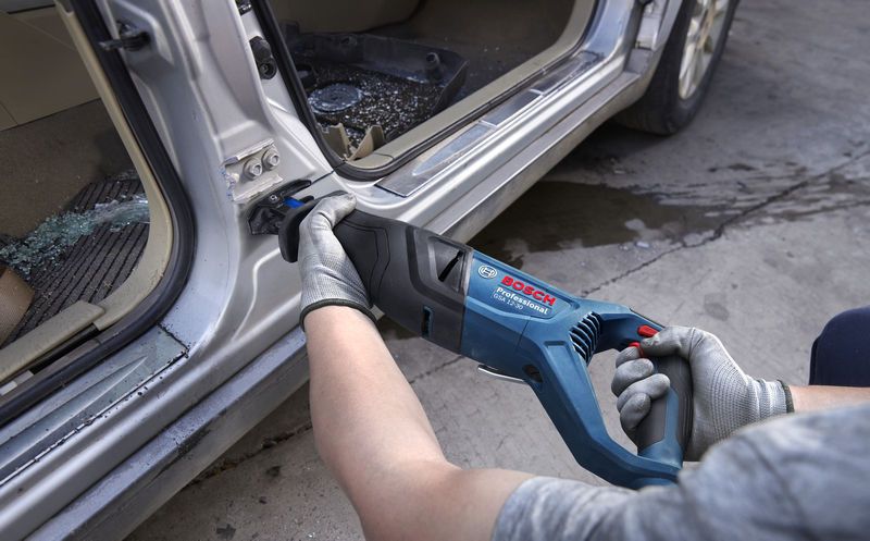 一名佩戴安全设备的人员使用往复锯切割车门框上的金属。.