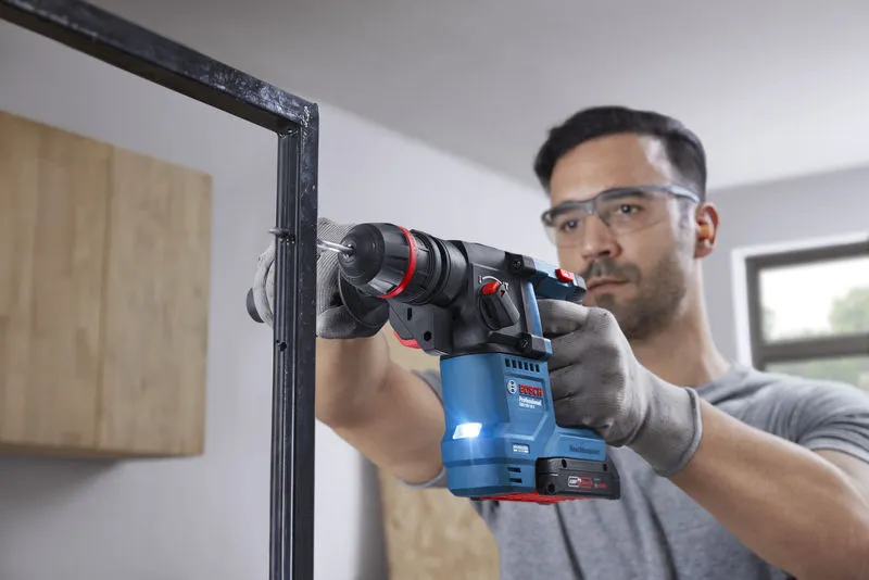 一名佩戴安全设备的人员使用无绳旋转锤在金属框架上钻孔。.