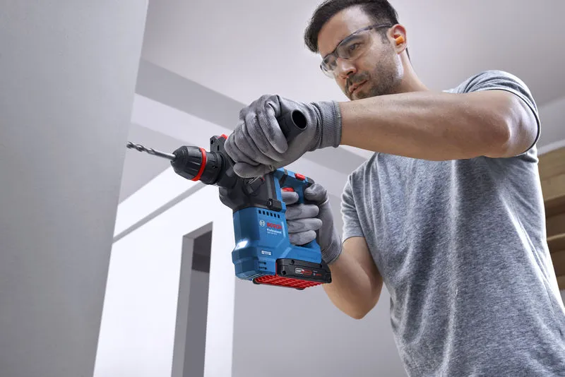 一名佩戴安全设备的人员使用无绳旋转锤在混凝土墙上钻孔。.