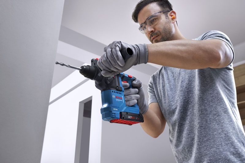 佩戴安全设备的人员使用旋转锤在墙上钻孔。.