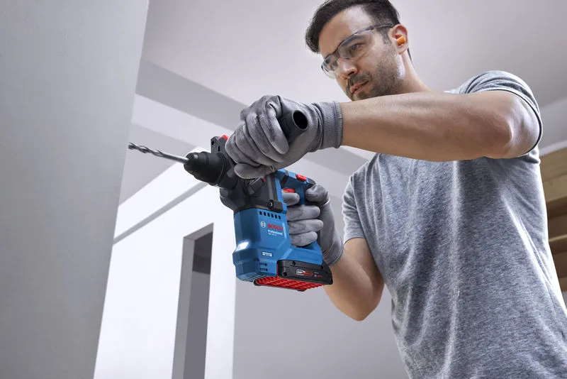 佩戴安全设备的人员使用旋转锤在墙上钻孔。.