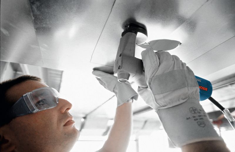 一名佩戴安全设备的人使用剪刀剪断一块金属板。