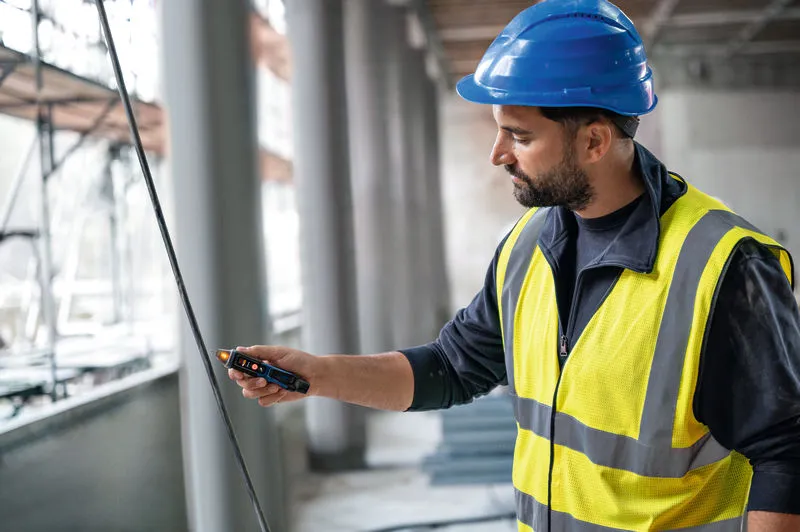 一名佩戴安全设备的人员正在使用非接触式电压测试仪测试电缆。.