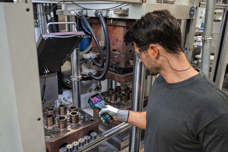 一名佩戴安全设备的人员正在使用热像仪检查工业机械。.