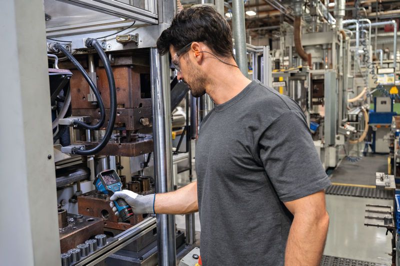 一名佩戴安全防护装备的人员正在使用热成像仪检查工业机械。