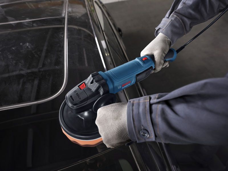 一名佩戴安全设备的人员正在使用电动抛光机抛光汽车车顶。.