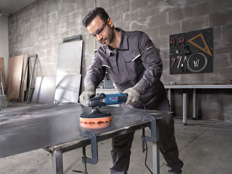 一名佩戴安全设备的人正在用电动工具抛光金属板。.