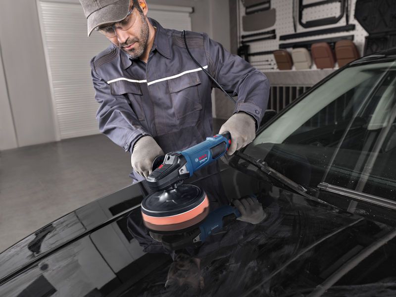 一名佩戴安全设备的人员正在使用电动抛光机抛光汽车引擎盖。.