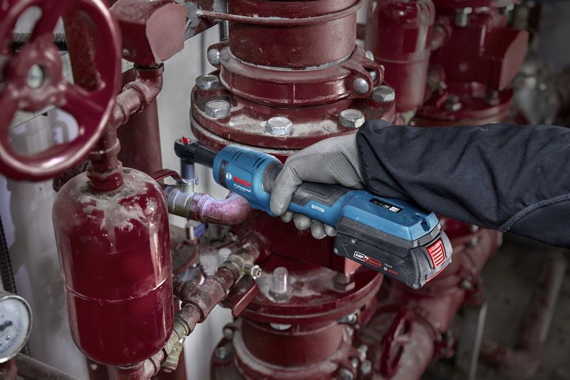 一名佩戴安全设备的人员使用无绳棘轮扳手对工业管道进行操作。.