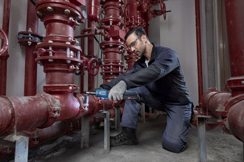 一名佩戴安全设备的人员使用无绳棘轮扳手操作红色管道系统。.