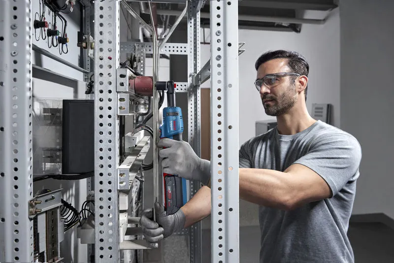 一名佩戴安全设备的人员在金属架上使用无绳棘轮扳手。.