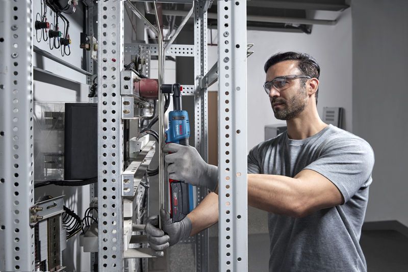 一名佩戴安全设备的人员在金属架上使用无绳棘轮扳手。.