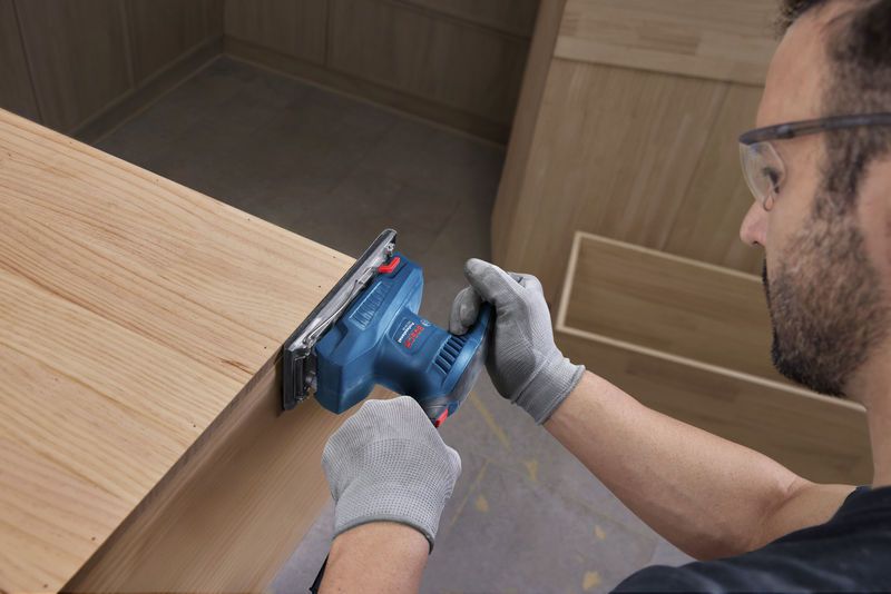 一名佩戴安全设备的人员正在使用轨道砂光机打磨木质表面。.