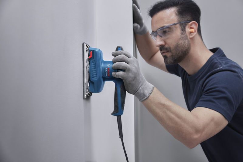 一名佩戴安全设备的人员正在使用轨道式打磨机打磨墙壁。.