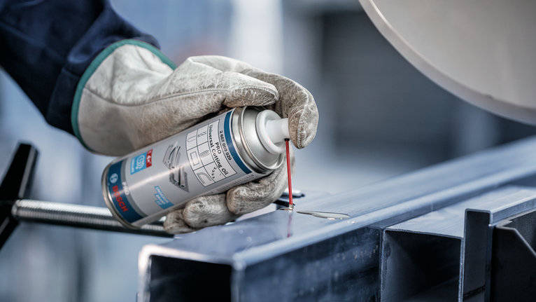 佩戴安全设备的人员将润滑剂喷洒到金属梁上。