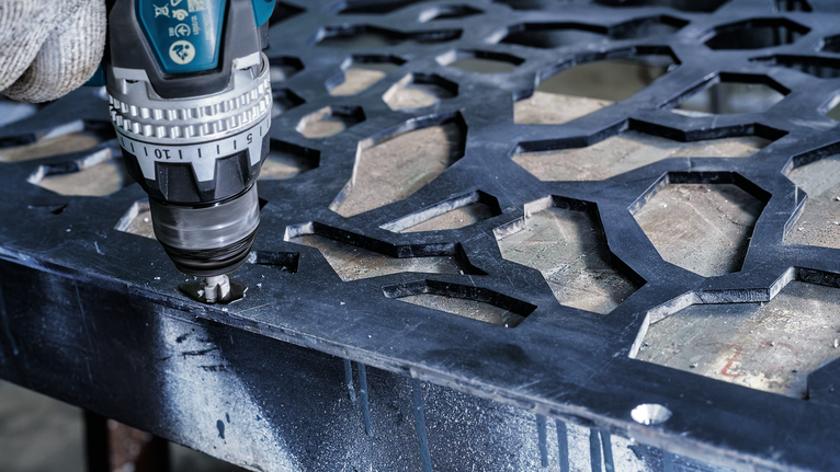 佩戴安全设备的人员使用无绳电钻在金属板上钻孔。.