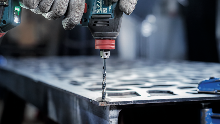 佩戴安全设备的人员在金属板上钻孔。