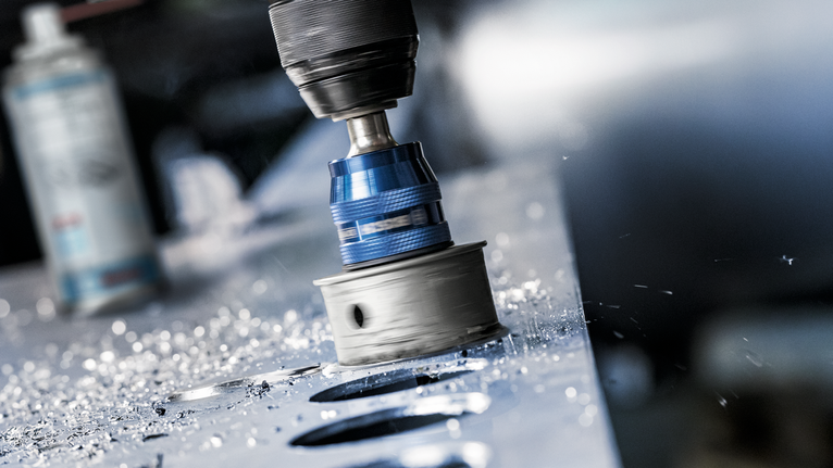 孔锯在金属板上钻出圆形孔，周围散落着金属屑。