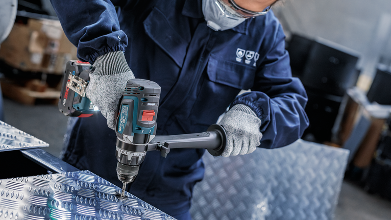 一名佩戴安全设备的人员正在一块有图案的金属板上钻孔。
