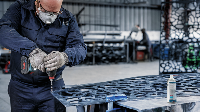 一名佩戴安全设备的人员在车间使用电动工具钻金属。