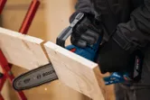 一名佩戴安全设备的人员使用无绳修枝锯切割木板。.